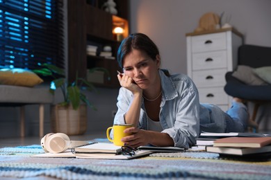 Photo of Tired student with cup of drink preparing for exam on floor at home