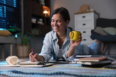 Photo of Happy student with cup of drink preparing for exam on floor at home