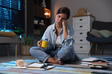 Photo of Tired student with cup of drink preparing for exam on floor at home