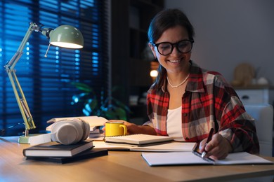 Photo of Happy student with cup of drink preparing for exam at wooden desk indoors