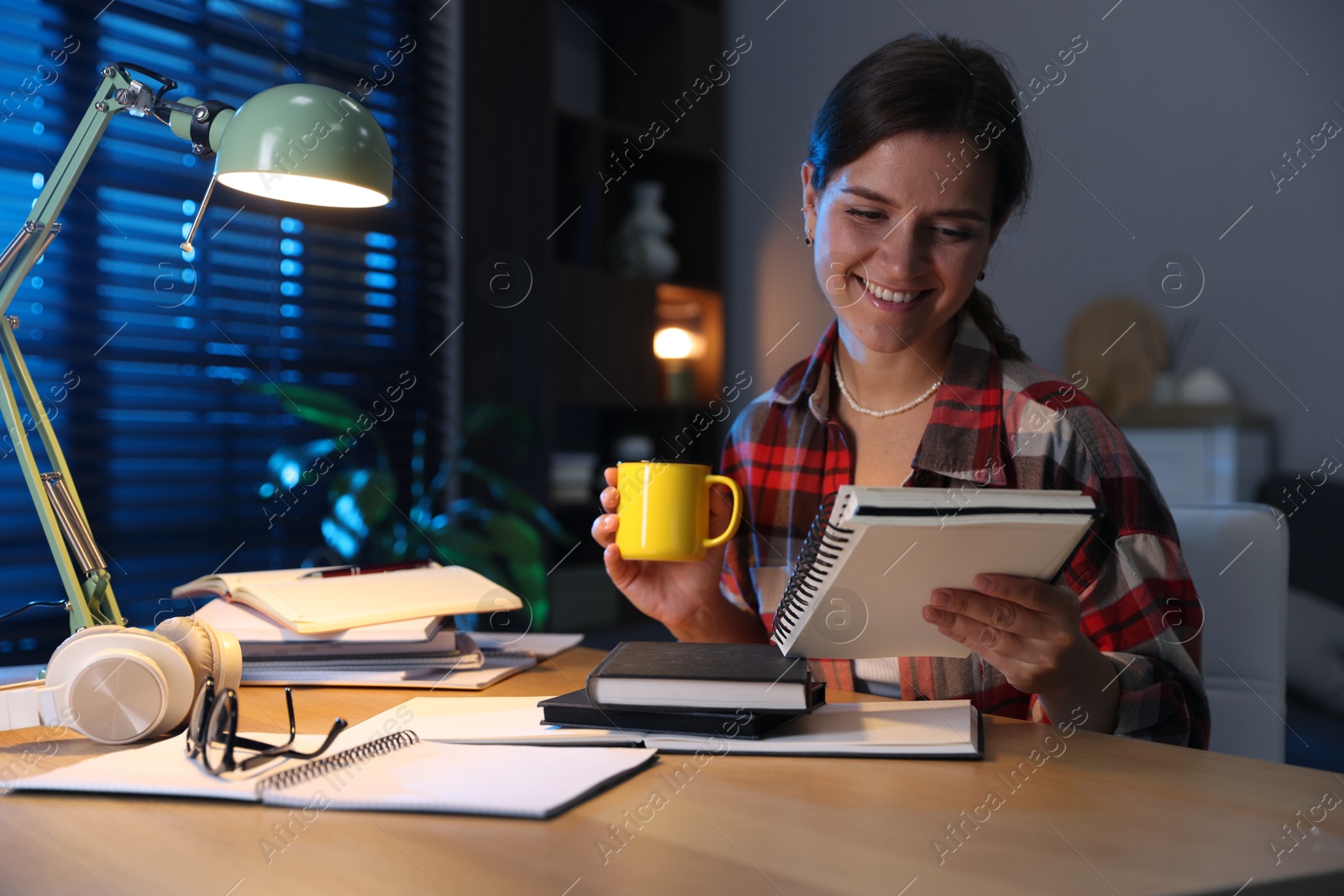 Photo of Happy student with cup of drink preparing for exam at wooden desk indoors