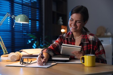 Photo of Happy student preparing for exam at wooden desk indoors
