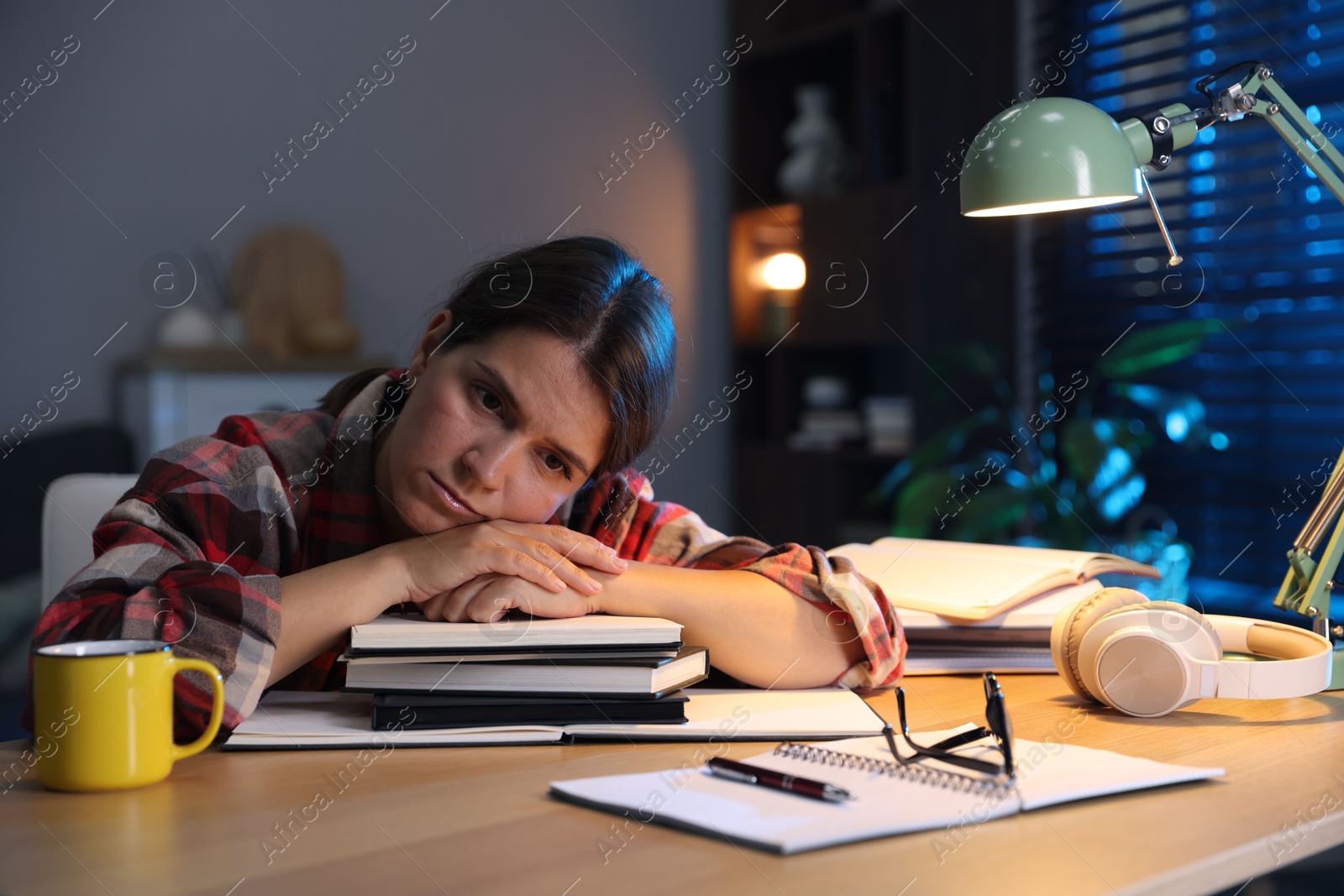 Photo of Tired student preparing for exam at wooden desk indoors