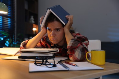 Photo of Tired student preparing for exam at wooden desk indoors