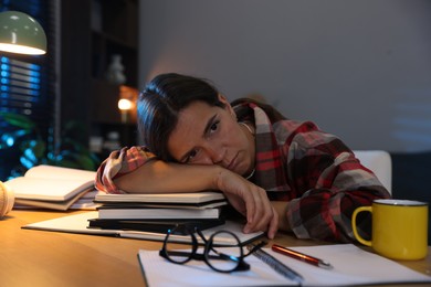 Photo of Tired student preparing for exam at wooden desk indoors