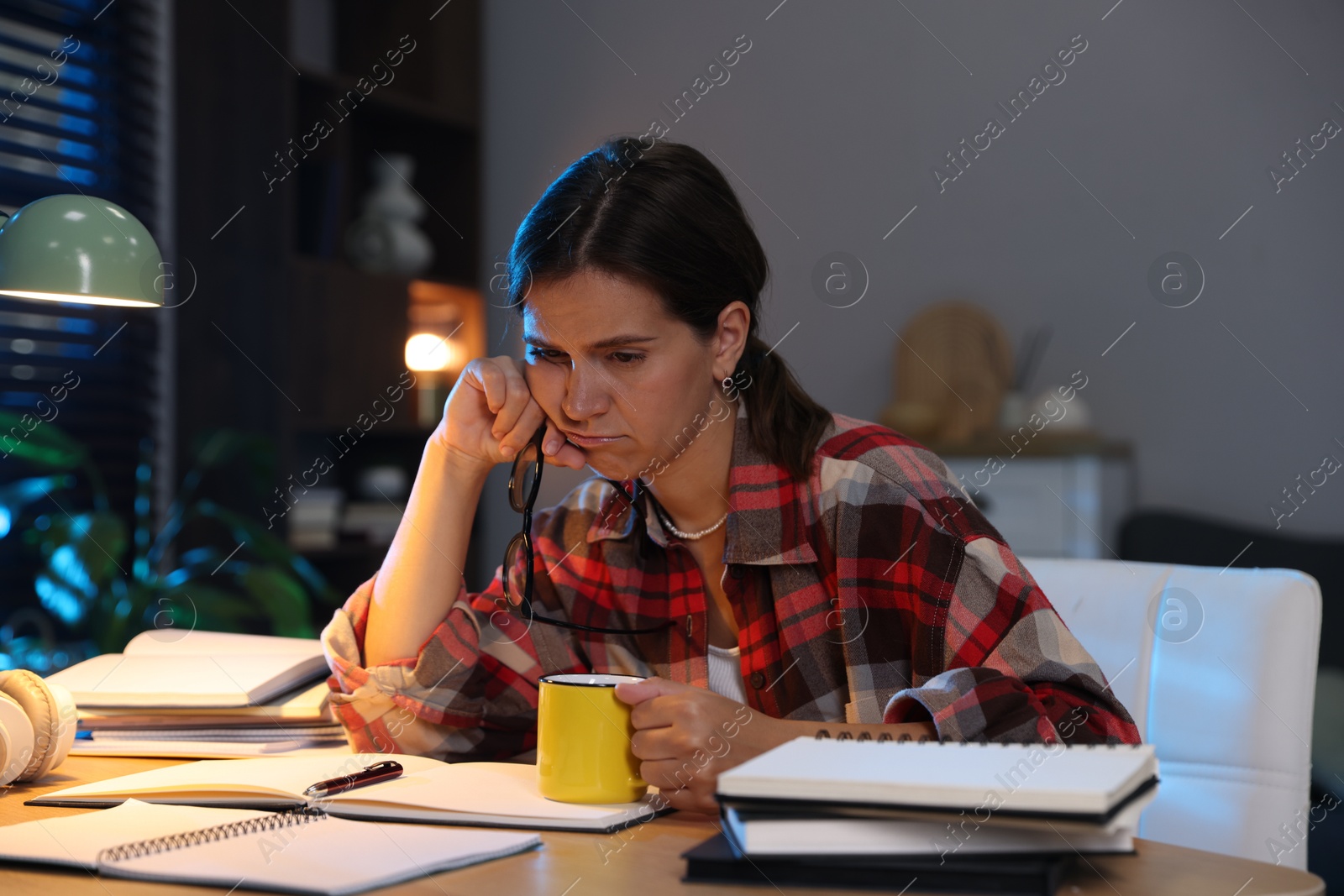 Photo of Tired student with cup of drink preparing for exam at wooden desk indoors