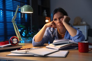 Photo of Tired student preparing for exam at wooden desk indoors
