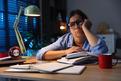 Photo of Tired student preparing for exam at wooden desk indoors