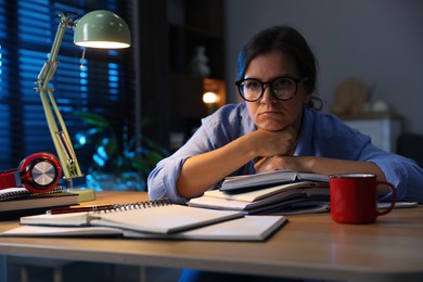 Photo of Tired student preparing for exam at wooden desk indoors