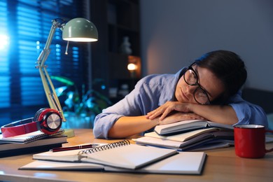 Photo of Tired student preparing for exam at wooden desk indoors
