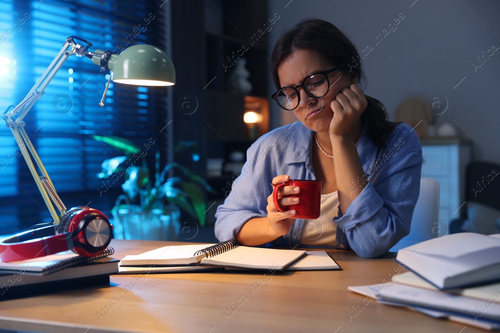Photo of Tired student with cup of drink preparing for exam at wooden desk indoors