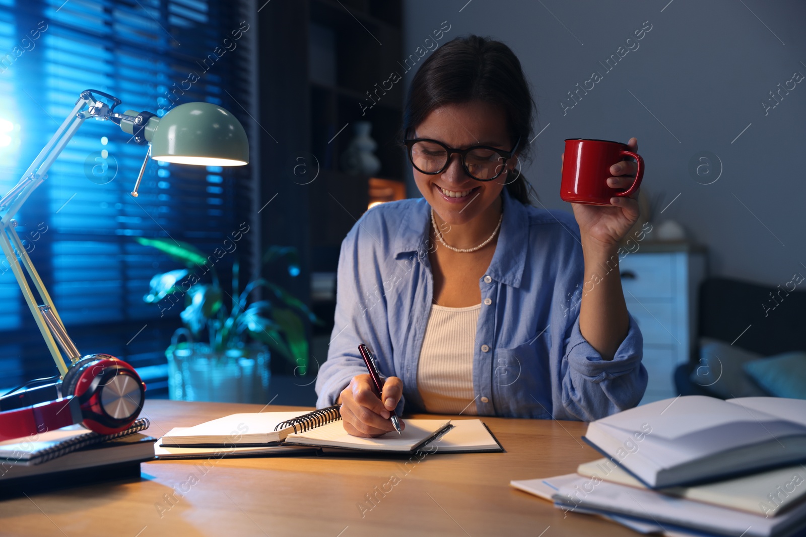 Photo of Happy student with cup of drink preparing for exam at wooden desk indoors