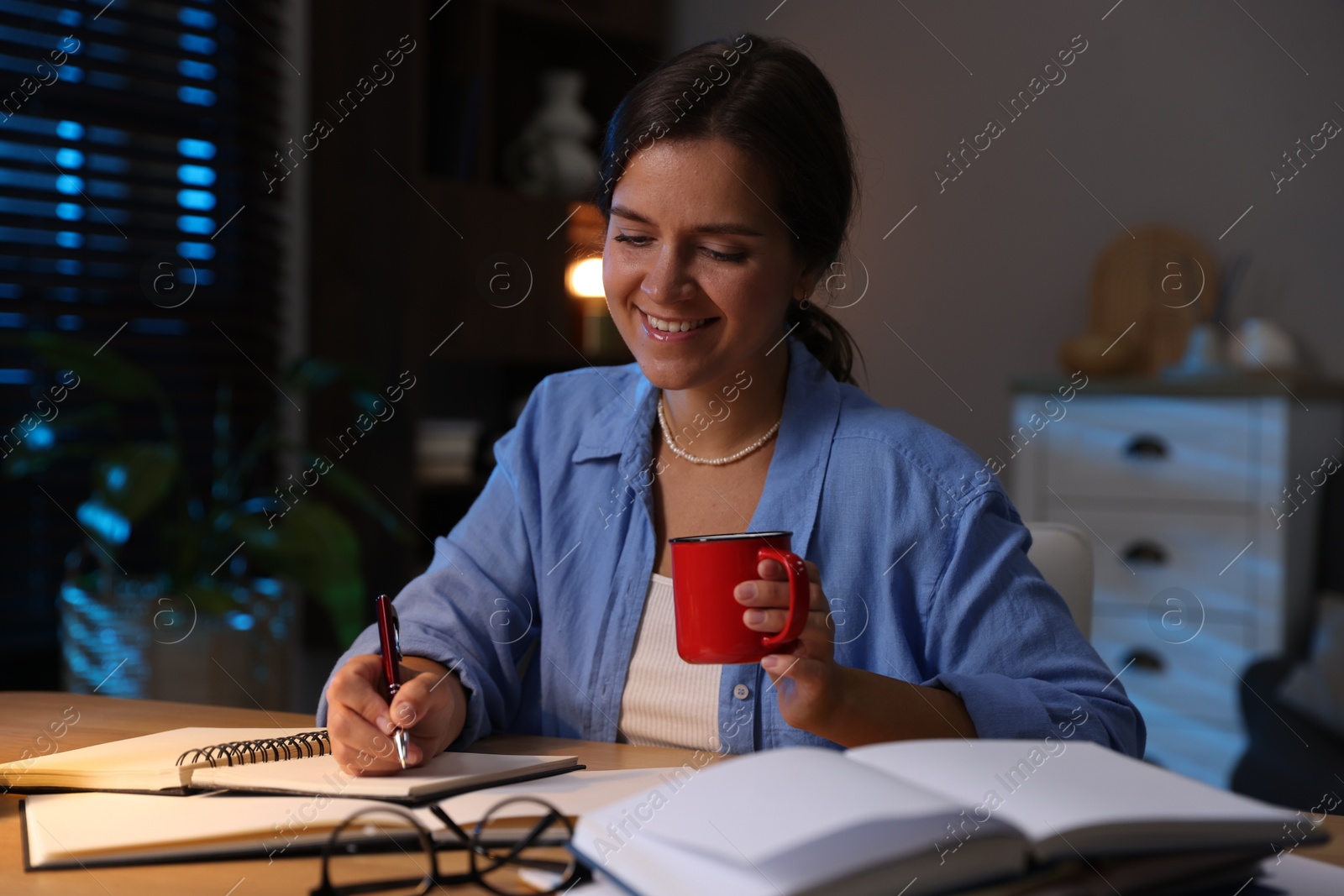 Photo of Happy student with cup of drink preparing for exam at wooden desk indoors
