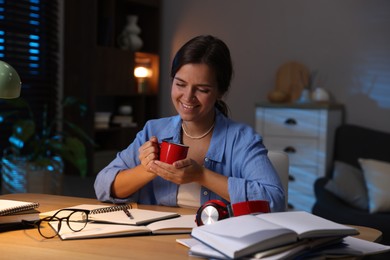 Photo of Happy student with cup of drink preparing for exam at wooden desk indoors