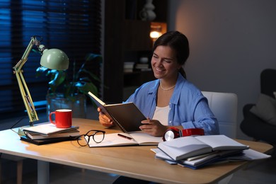 Photo of Happy student preparing for exam at wooden desk indoors