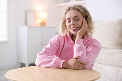 Photo of Happy young woman sitting at wooden table and looking at something indoors