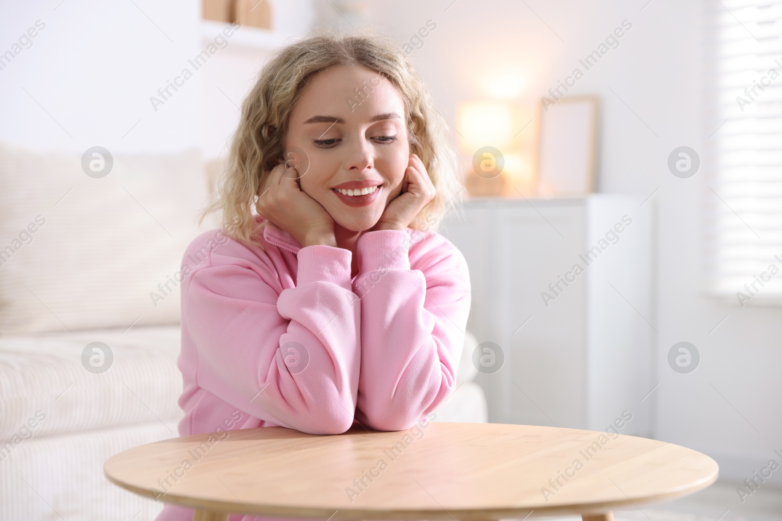Photo of Happy young woman sitting at wooden table indoors