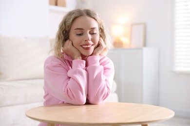 Photo of Happy young woman sitting at wooden table indoors