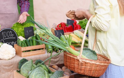 Photo of Woman choosing fresh vegetables from stall at farmer's market, closeup