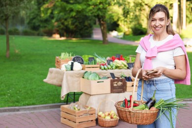 Photo of Woman with different fresh vegetables in wicker basket at farmer's market