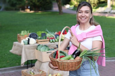 Photo of Woman with different fresh vegetables in wicker basket at farmer's market