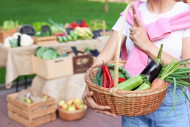 Photo of Woman with different fresh vegetables in wicker basket at farmer's market, closeup