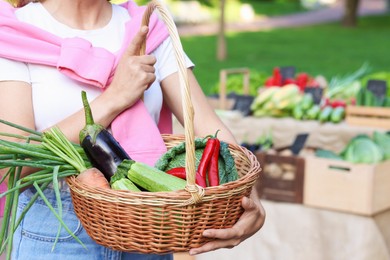 Photo of Woman with different fresh vegetables in wicker basket at farmer's market, closeup