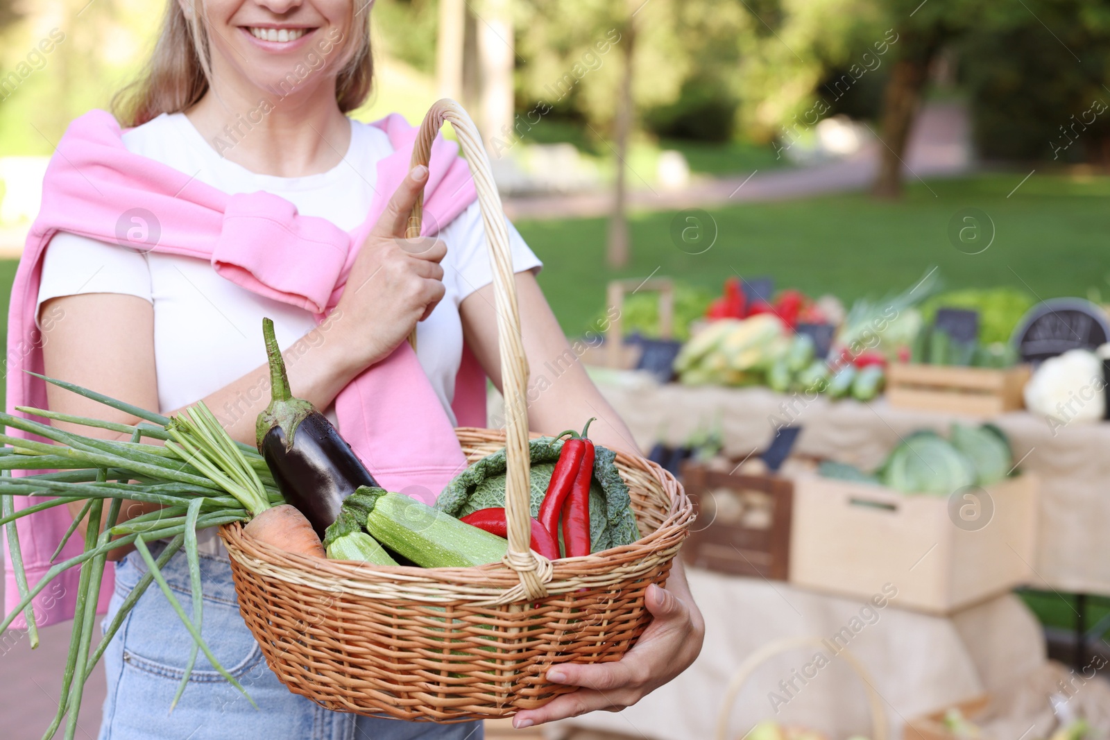 Photo of Woman with different fresh vegetables in wicker basket at farmer's market, closeup