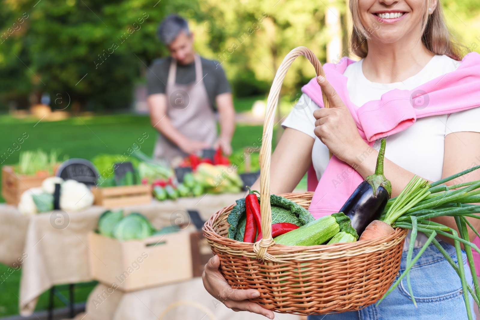 Photo of Woman with different fresh vegetables in wicker basket at farmer's market, closeup