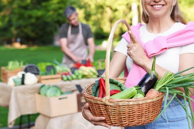 Photo of Woman with different fresh vegetables in wicker basket at farmer's market, closeup