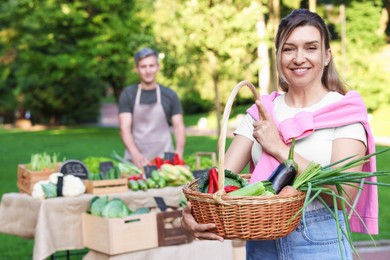 Photo of Woman with different fresh vegetables in wicker basket at farmer's market, selective focus