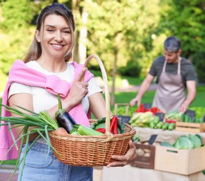 Photo of Woman with different fresh vegetables in wicker basket at farmer's market, selective focus
