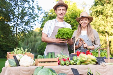 Photo of Happy farmers holding products near stall with different fresh vegetables at market