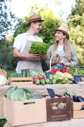 Photo of Happy farmers holding products near stall with different fresh vegetables at market