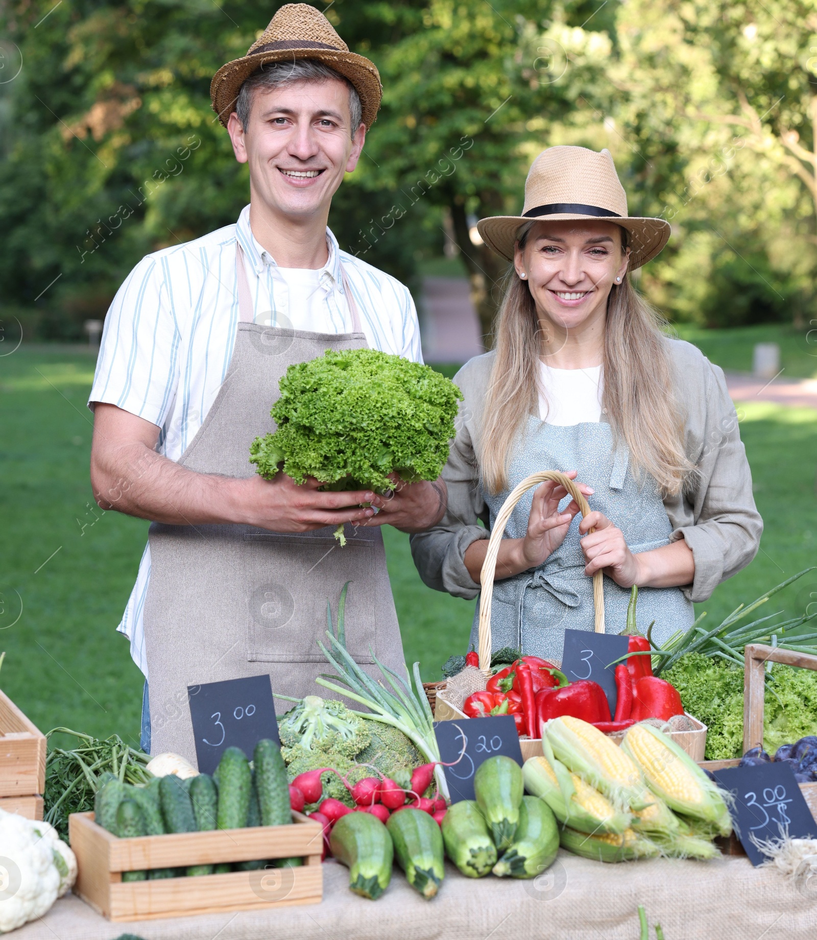 Photo of Happy farmers holding products near stall with different fresh vegetables at market