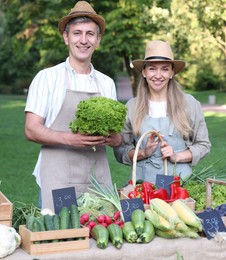 Photo of Happy farmers holding products near stall with different fresh vegetables at market
