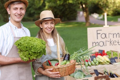 Photo of Happy farmers holding products near stall with different fresh vegetables at market
