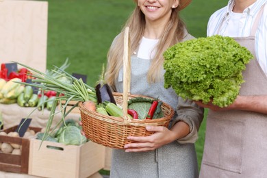 Photo of Farmer holding products near stall with different fresh vegetables at market, closeup