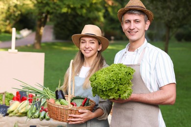 Photo of Happy farmers holding products near stall with different fresh vegetables at market
