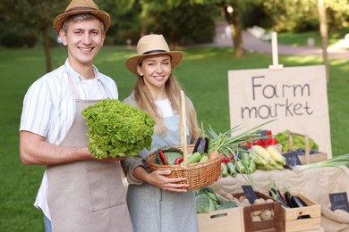 Photo of Happy farmers holding products near stall with different fresh vegetables at market
