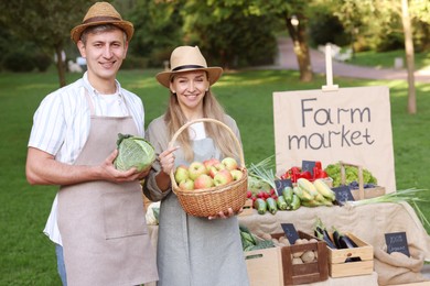 Photo of Happy farmers with products near stall with different fresh vegetables at market