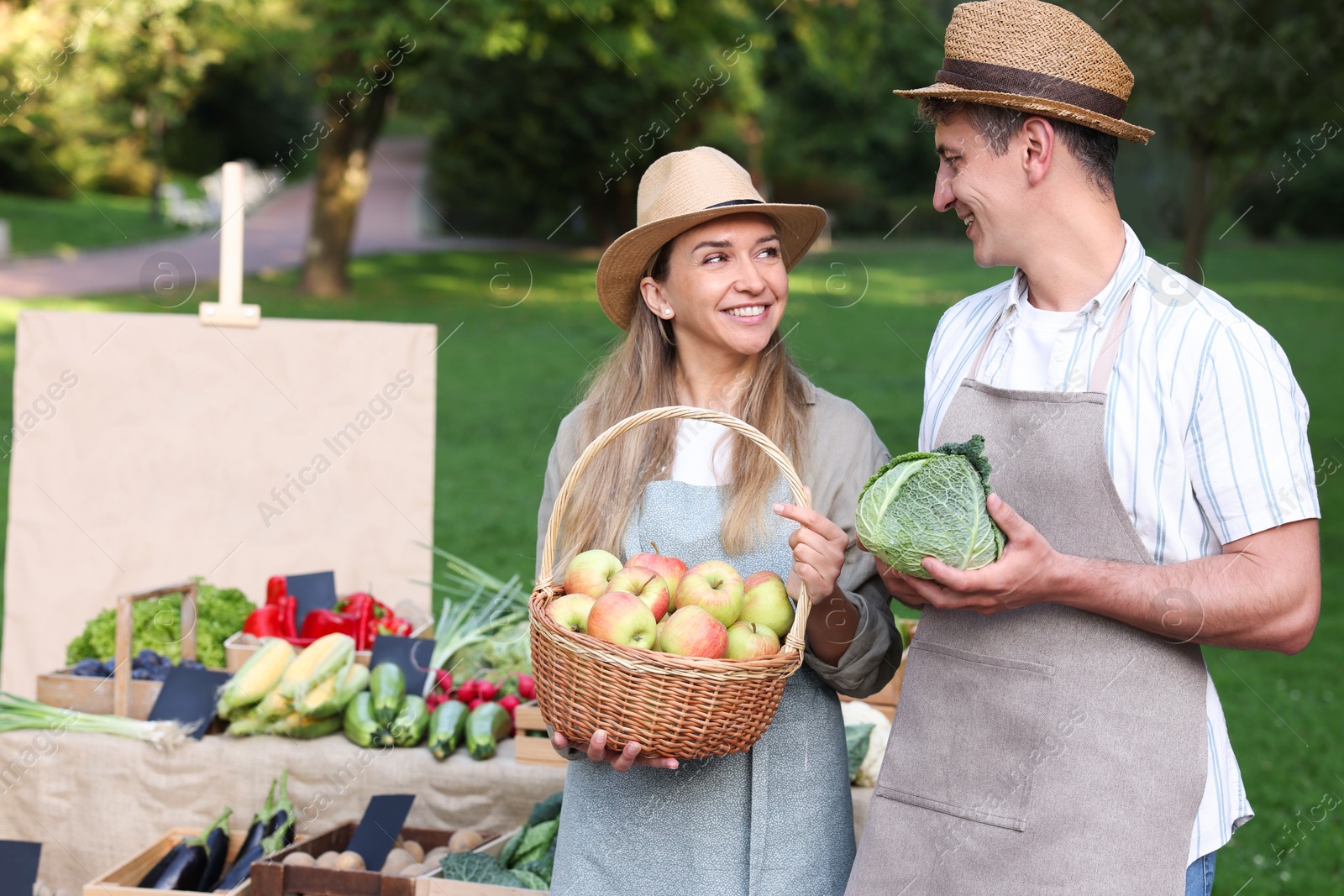 Photo of Happy farmers with products near stall with different fresh vegetables at market