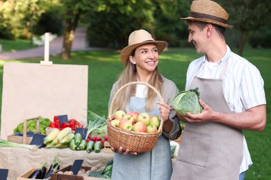 Photo of Happy farmers with products near stall with different fresh vegetables at market