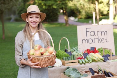 Photo of Farmer with apples in wicker basket near stall at market