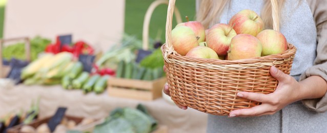 Photo of Farmer with apples in wicker basket near stall at market, closeup