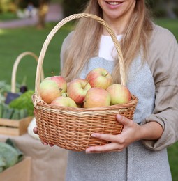 Photo of Farmer with apples in wicker basket near stall at market, closeup