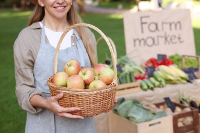 Photo of Farmer with apples in wicker basket near stall at market, closeup