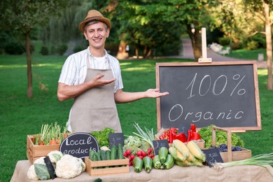 Photo of Happy farmer near stall with different fresh vegetables at market