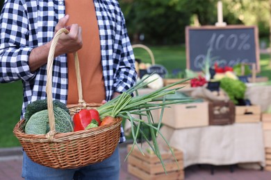 Photo of Man with different vegetables in wicker basket at farmer's market, closeup