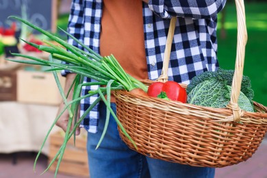 Photo of Man with different vegetables in wicker basket at farmer's market, closeup